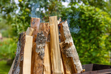 Burning pack of birch firewood in an old rusty grill in the backyard
