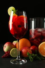 Glass and jug of Red Sangria with fruits on black table