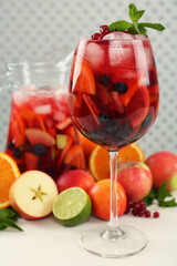 Glass and jug of Red Sangria with fruits on white wooden table