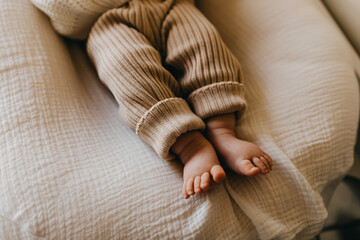 Closeup of barefoot baby feet wearing knitted brown pants.