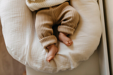Closeup of baby feet in knitted brown pants. - obrazy, fototapety, plakaty