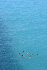 Una persona nuota distante dal gruppo di amici e amiche in mezzo al mare facendo snorkeling  e nuotando nel mare calmo. Ripresa aerea con drone dall'alto.