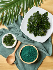 Top view laminaria or kelp seaweed and spirulina powder in wood bowl and spoon background. flat lay spirulina powder with konbu and alga food on wood table background. © boommaval
