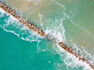 aerial view of the stormy blue and green sea divided by a diagonal of rocks