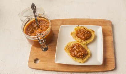 Open jar of chutney on  cutting board on and a plate of zucchini pancakes  table.