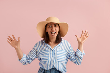 Obraz na płótnie Canvas Scared alarmed annoyed woman with dark hair screams loudly in fear, keeps mouth wide open, keeps palms raised, wears straw hat, striped shirt, jeans, on pink background. Summer emotions concept.