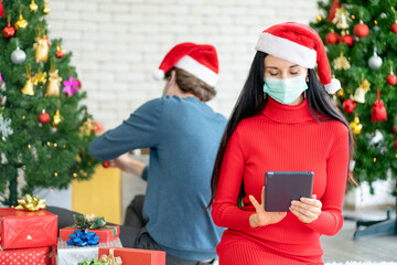 Obraz na płótnie Canvas Caucasian woman with hygiene mask choose the gift from online shop via tablet for celebration of Christmas during Covid-19 pandemic and new normal lifestyle to stay at home.