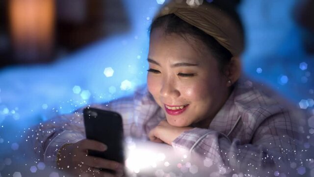 3d render glowing flares and shimmer vfx on young beautiful and happy sweet Asian Korean woman in headband and pajamas enjoying with hand phone in bed at night