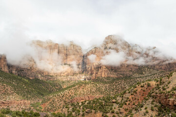The mountains of Zion National Park in Utah with a heavy overcast and clouds dramatically passing in from of the peaks.  This unusual weather provides a dramatic feel and a sense of calm.