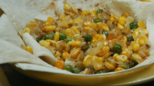 a person's hands stir and pick fried Asian vegetables on pita bread in a yellow bowl with hashi chopsticks and eat. Vegetarian food. Close-up