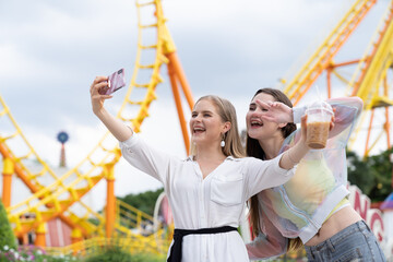 Two young female tourists at the amusement theme park on Roller coaster background. tourism,...