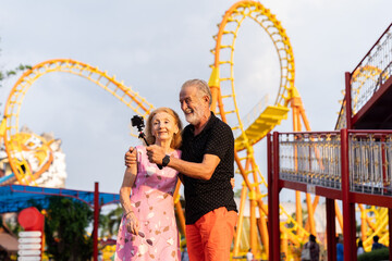 Happy senior couple embracing and talking selfie at the amusement theme park. Smiling elderly...