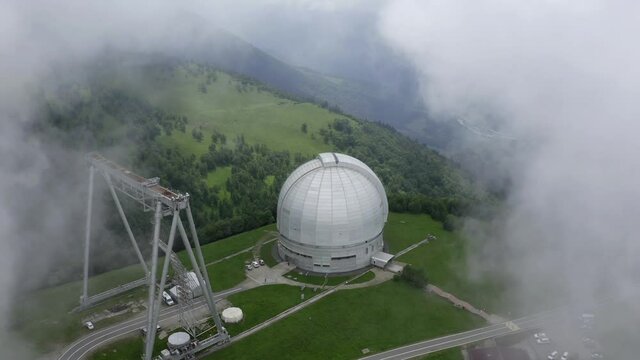Nizhny Arkhyz, Russia - June 26, 2021: Aerial zoom out view of Astrophysical observatory of Russian Academy of Sciences in Caucasus. BTA tower. Drone goes back in flowing clouds. Scenic landscape.