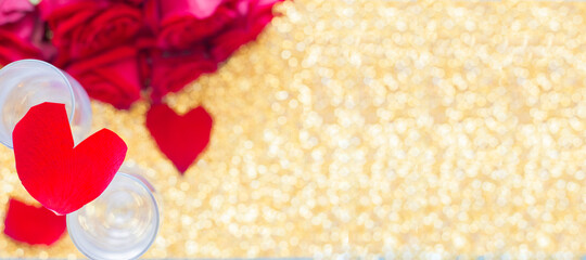 A heart of rose petals lies on two glasses, at the bottom there is a blurry bouquet of red roses and hearts on a bright gold background. top view, flat lay, copy space, isolate.