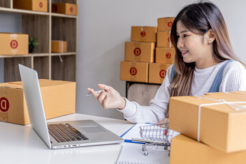 A woman who owns an e-commerce website is video calling chatting with business partners and packing parcels, she is discussing marketing plans to increase sales. Online selling concept.