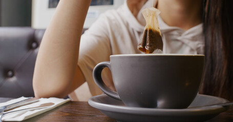 Woman dipping tea bag in cup at restaurant