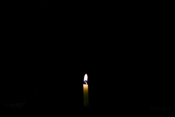 A lonely burning candle in pitch darkness. A weak candle light will illuminate only the wax candle...