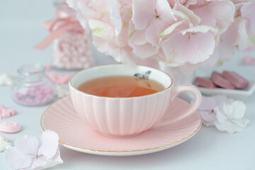Fototapeta na wymiar Pink cup of tea and sweets on the table with pink hydrangea