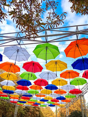 Fototapeta na wymiar Autumn-themed umbrellas hang over the park alley