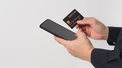 Hand is holding mobile phone and black credit card on white background.