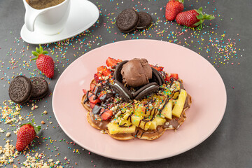 Heart waffle with pineapple and strawberry with gummy candy and ice cream on it.