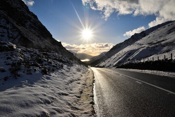 a road going down a valley surrounded by mountains and snow