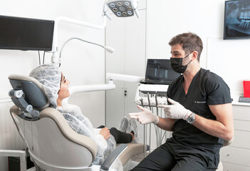 Dentista habla con su paciente mujer, explicandole que trabajo realizará en su boca - obrazy, fototapety, plakaty