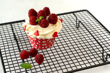 Cupcake with cream and raspberries and hearts on the wire rack. Dessert preparation. Copy space. On white background. Delicious delicacy. Muffin with cream. Cake.