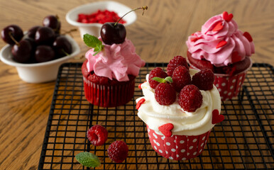 Red velvet cupcakes with cream, raspberries and cherries, decorated with hearts. Preparation for the holiday. Sweet dessert. A confectionery stand stands on a wooden table.