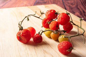 Cherry tomatoes, stale cherry tomatoes still rotting in the vine on wooden surface, dark...
