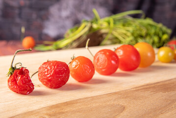 Cherry tomatoes, cherry tomatoes lined up from greenest to rotting through ripe on a wood, dark background, selective focus.
