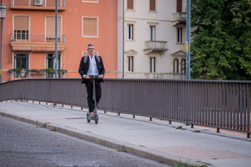 Handsome businessman in suit riding an electric scooter while commuting to work in the city. Ecological transport concept