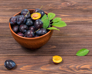 Fresh ripe plum fruits whole and chopped with leaves in a bowl on a wooden brown table. Summer harvest.