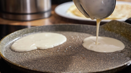 Unrecognizable woman pours screed dough into a hot frying pan.