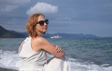young girl in a white dress sits on the seashore