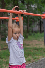 Obraz premium cheerful naughty girl 6-7 years old plays on the playground and hangs on the uneven bars