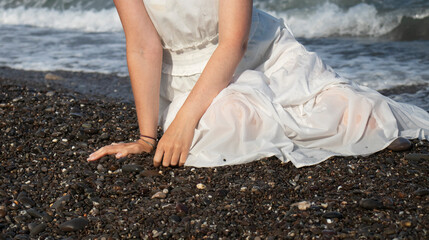 young girl in a white dress sits on the seashore