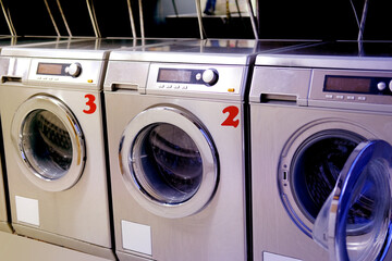 row of washing machines in public city self-service laundromat, clean linen concept, washing clothes, bachelor life