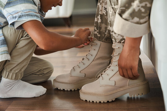 Woman wearing military uniform sitting at the sofa while her son tie her shoe laces