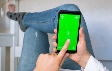 phone with Green screen and chroma key. Woman at Home Lying on a Couch using Smartphone with Green Mock-up Screen, Doing Swiping, Scrolling Gestures. Girl Using Mobile Phone
