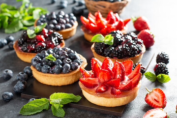 Strawberries, blueberries, blackberries tartlets with chocolate ganache, fresh berries and mint leaves. Fresh fruit tart, freshly homemade fruit cake on a table