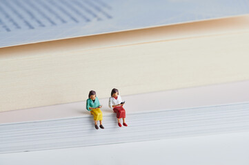 two miniature women sitting on books and are reading