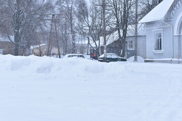 Fototapeta na wymiar Winter. Snowing. Snowdrifts lie on a rural street, cars are parked in the parking lot.