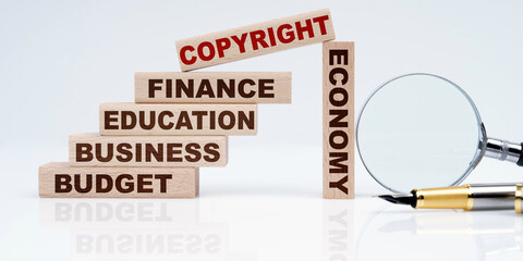 Magnifier, pen and wooden blocks with the text - Business, Budget, Education, Economics, Finance and COPYRIGHT