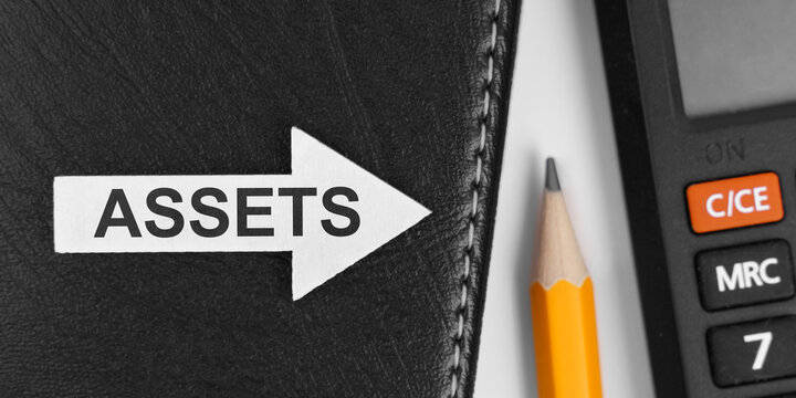 Next to the calculator and pencil there is a notebook on which a white arrow with the inscription - ASSETS