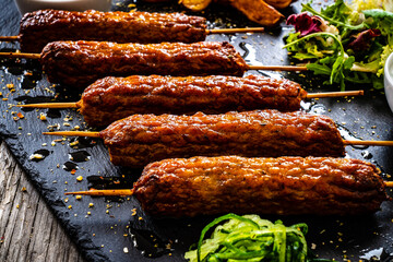 Cevapcici - Balkan shashlik served with baked potatoes, fresh green vegetables and tzatziki on black stone plate

