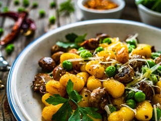Gnocchi with fried white mushrooms, green peas, parmesan and parsley on wooden table
