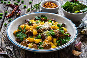 Gnocchi with fried white mushrooms, green peas, parmesan and parsley on wooden table
