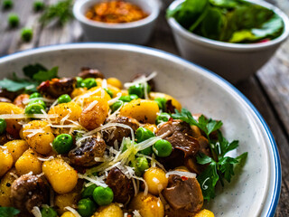 Gnocchi with fried white mushrooms, green peas, parmesan and parsley on wooden table
