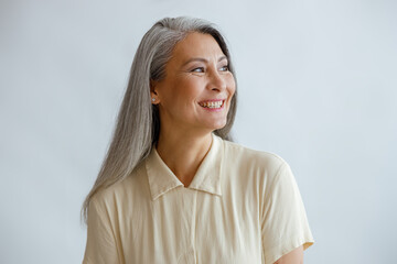 Joyful long haired middle aged lady wearing beige blouse stands on light background in studio....